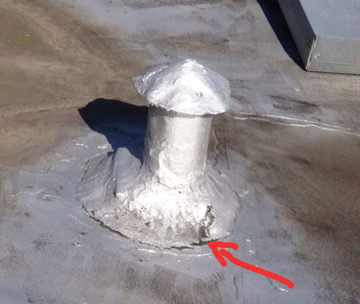 Retail aluminum-fibered roof patch shrinking and separating from a roof penetration, opening a leak where the red arrow points