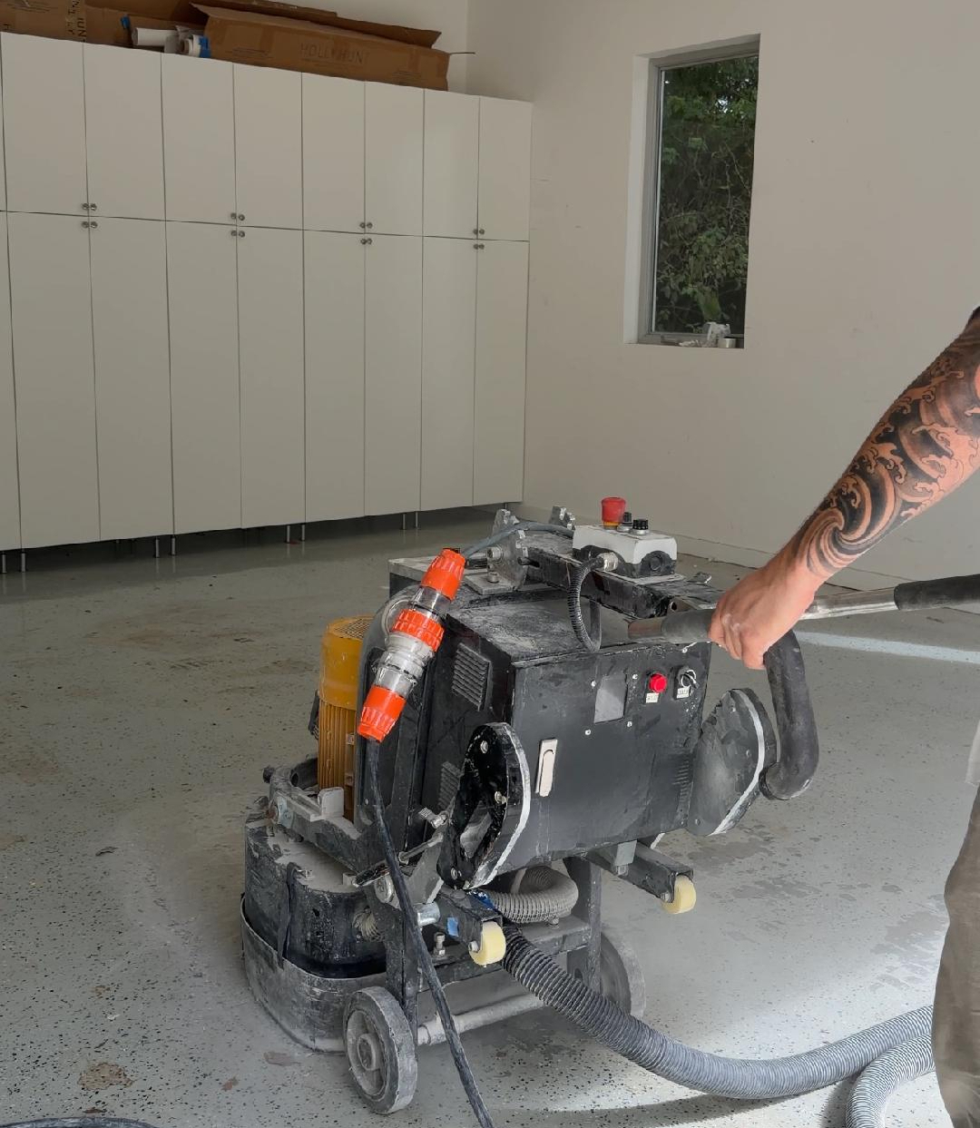 Contractor diamond-grinding a failed epoxy floor down to bare concrete before it can be recoated