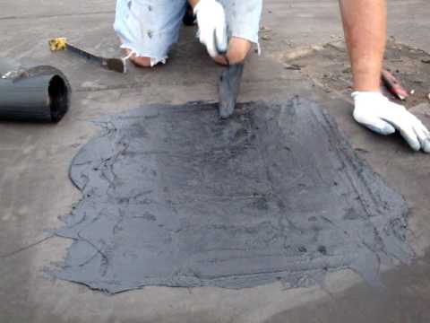 Applying black tar-based roof cement such as Karnack to a roof repair